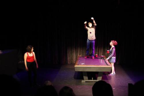 Photo by Robert Schulz SHE (Claire Rigsby) and ALEX (Tatiana Ray) watch as HE (James Henderson) pins a dollar to the ceiling. 